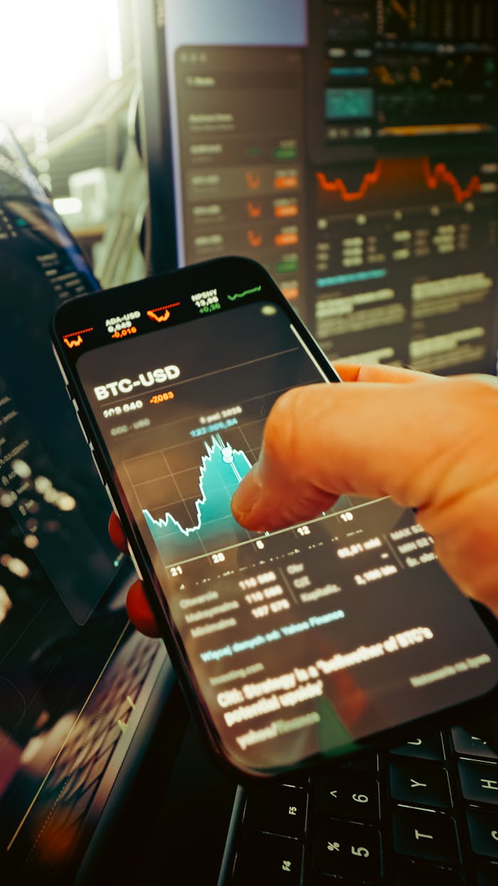 project-01-b A hand holds a smartphone displaying BTC-USD chart amidst digital trading screens, highlighting crypto finance.